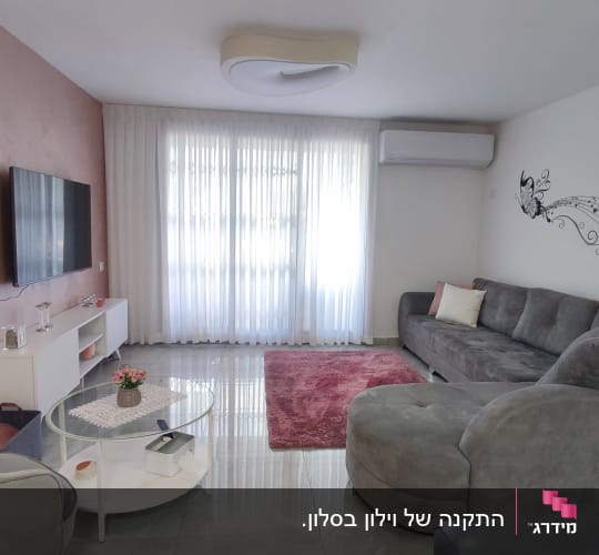וילון לבן שקוף תלוי על חלון גדול בסלון.